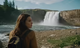 a girl wearing a backpack looks out at a waterfall