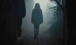 two people walking through a forest on a foggy day