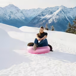 a woman sits in the snow on a pink sled
