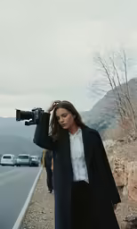 woman wearing black coat holding a camera standing near road