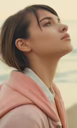 a woman standing by the water with her head turned to look off in order