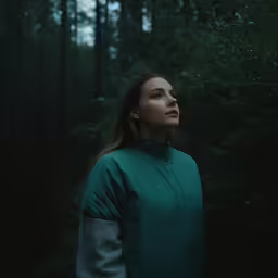 a woman stands in the woods staring out