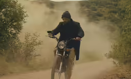 the man is riding his bike down the dirt road