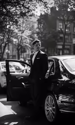 black and white photograph of a man in a suit next to his car