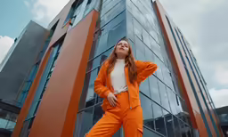a woman in an orange suit standing by a tall building