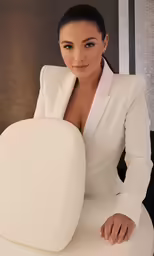a woman is sitting at a chair in a white suit