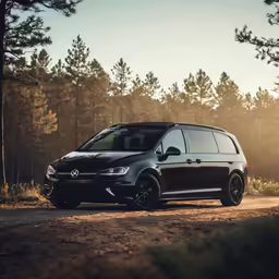 a black minivan parked in the middle of a forest