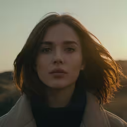 a woman with brown hair and a beige coat looking off into the distance