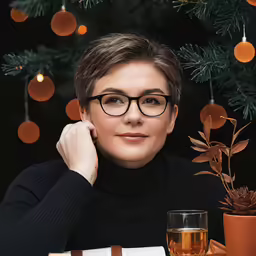 woman sitting at table with wine glass and candle, decorated tree behind her