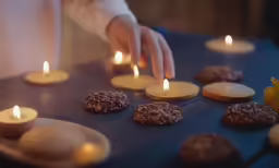a hand placing candles on cookies on a table