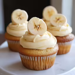 four cupcakes have bananas and frosting on top