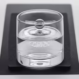 a clear glass with a silver handle is sitting on a black base