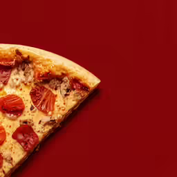 slice of pizza with several toppings on it on red surface