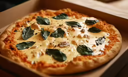 a pizza sits in a box with cheese and green leaves on top