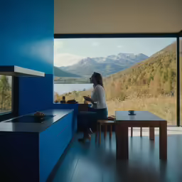 a woman sitting in front of a window with mountains behind her