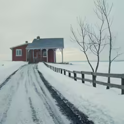 a snow covered dirt road leading to a red building