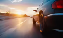 a car driving down a road with a setting sun in the background