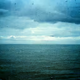 people riding bikes on the shore during the day,the ocean has gray clouds over it and is still dark