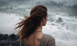 a young woman stares out into the ocean, while storm rolls in