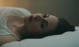 a woman laying in bed wearing white dress and looking up