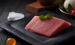 piece of raw fish sits on a slate plate next to fresh ingredients