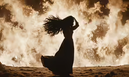 a woman dancing in front of a explosion of fire