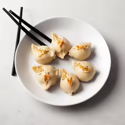 a white plate with five uncooked dumplings and black chopsticks