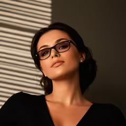 a beautiful woman in glasses leaning against a wall