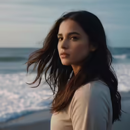 a young woman stands on a beach facing the ocean