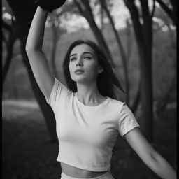 woman in white top and tan pants holding a hat up