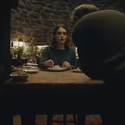 a young woman sitting down to eat dinner with a man in the background