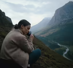 a woman is sitting on a cliff and talking on her cellphone