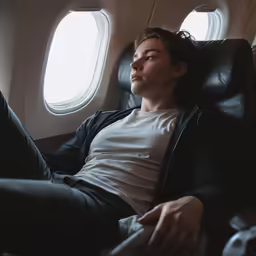 man in black leather pants sitting on a black leather seat on an airplane