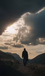a man is walking down a path towards the sun in the sky