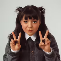 a young child wearing a tie is making a peace sign with their fingers