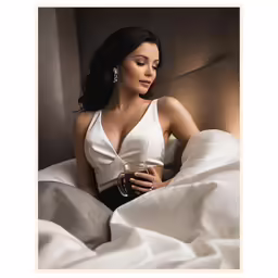 a woman sitting on a bed and holding a glass