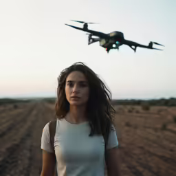 a girl standing in the middle of a field with a plane flying above
