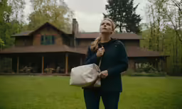 a woman holding a purse is walking out to the woods