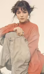 the young girl in an orange sweater is sitting on a wooden chair