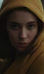 a young woman wearing a yellow hoody looks to the side
