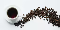 roasted coffee beans spilling out from a cup of coffee