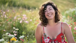 a beautiful woman in a field of wildflowers with a smile on her face,a smiling woman in a red dress sitting in a field