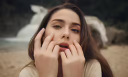 a girl sitting on the beach covers her face