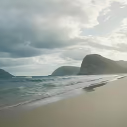 a beach with waves coming in to shore and mountains in the background
