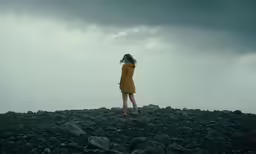 a woman wearing a yellow dress stands on rocks