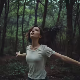 a young woman stands in the forest and looks upward to the sky
