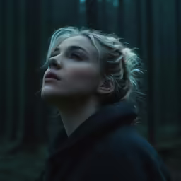 a woman with her eyes closed looking upward into the woods