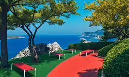 two park benches sit along a pathway in a garden near a scenic ocean