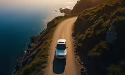 an aerial shot of a white truck driving down a dirt road