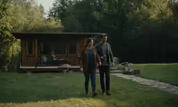 two people are walking towards the back of a house